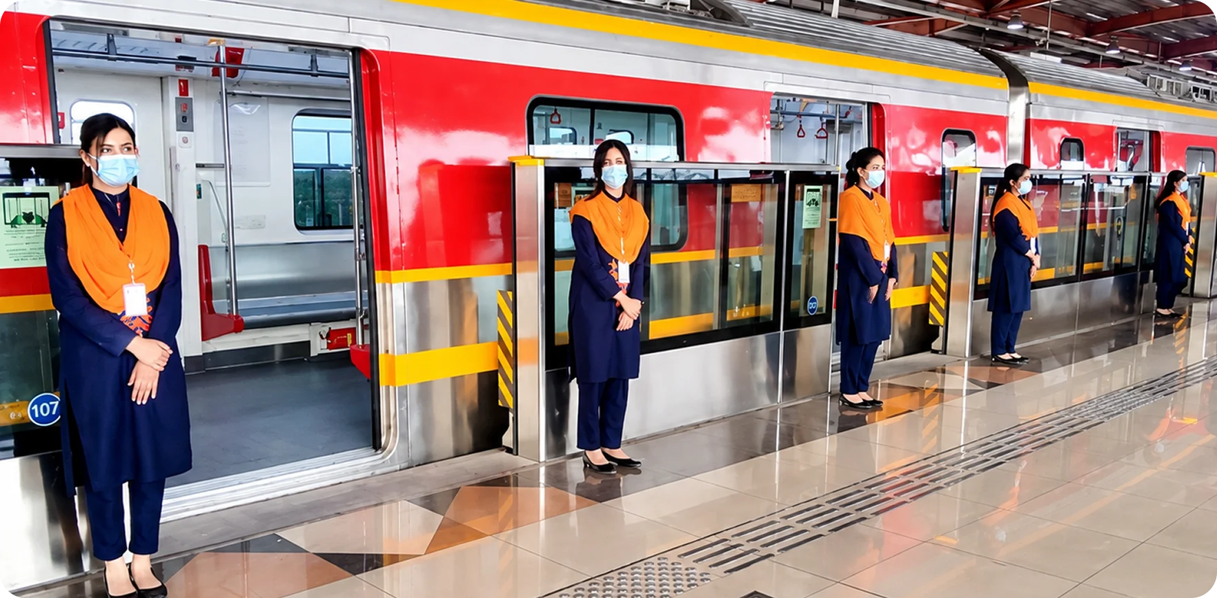 Orange Line Metro Train staff in orange and navy uniforms standing at the train doors on a station platform